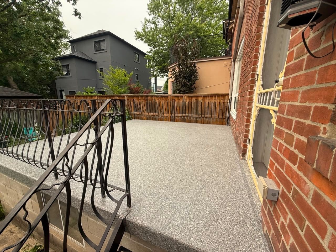 A raised rear patio in Toronto finished in a full-flake polyaspartic system, carried to the railing base and over the edge